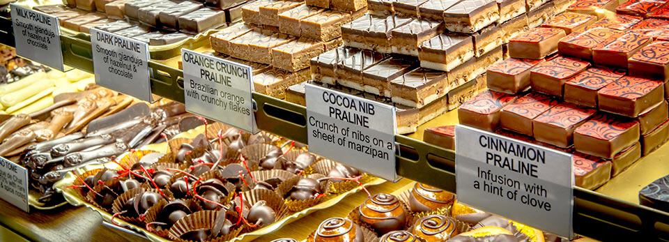 Glass display case filled with rows of handcrafted pralines and truffles with printed flavour labels at Highland Chocolatier.